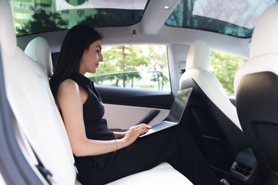 Photo of Woman using laptop in modern car, view from outside