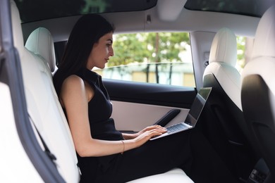 Photo of Woman using laptop in modern car, view from outside