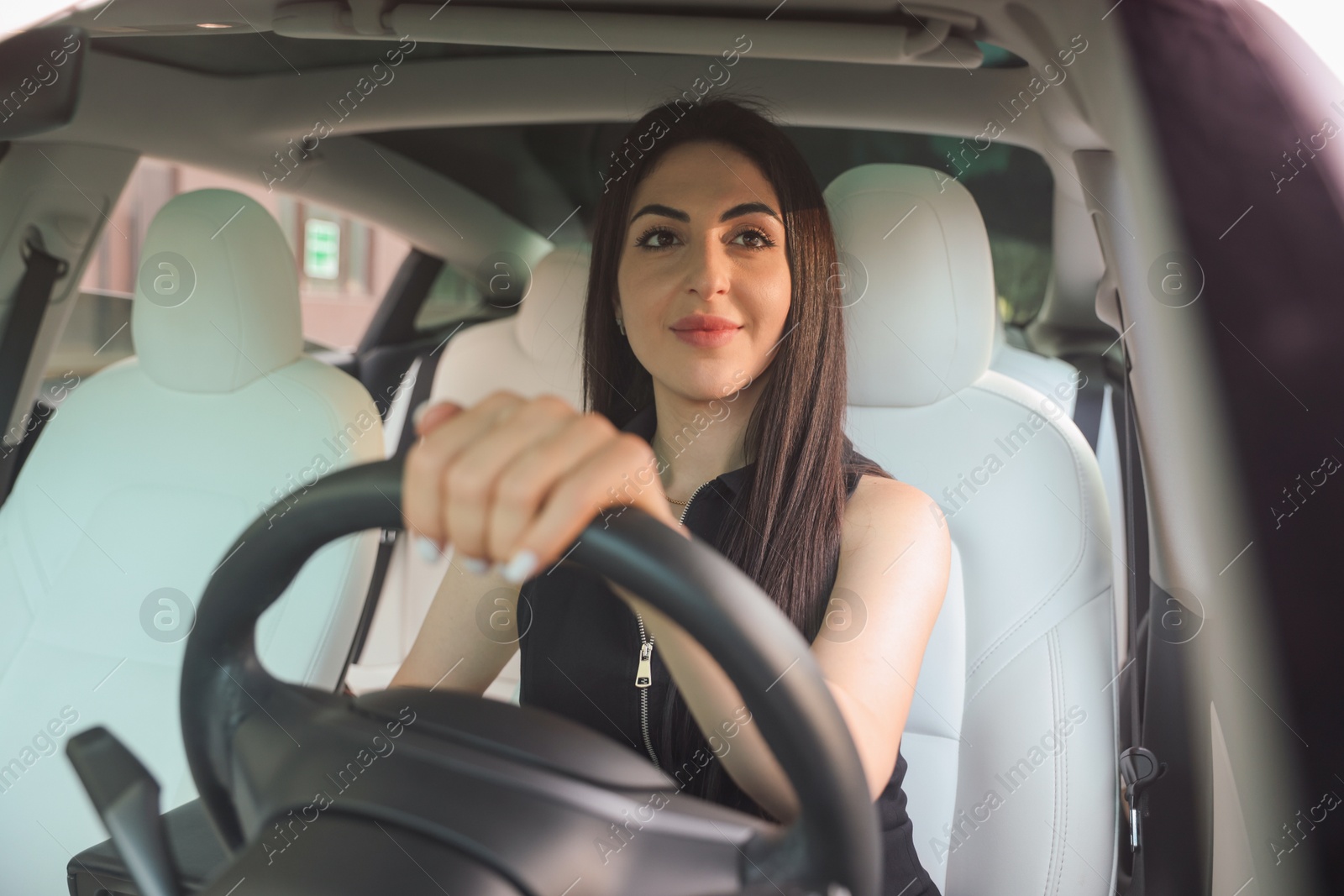 Photo of Woman behind steering wheel of modern car, view through windshield