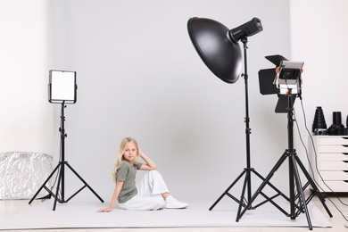 Photo of Little girl on light grey background in photo studio with professional equipment