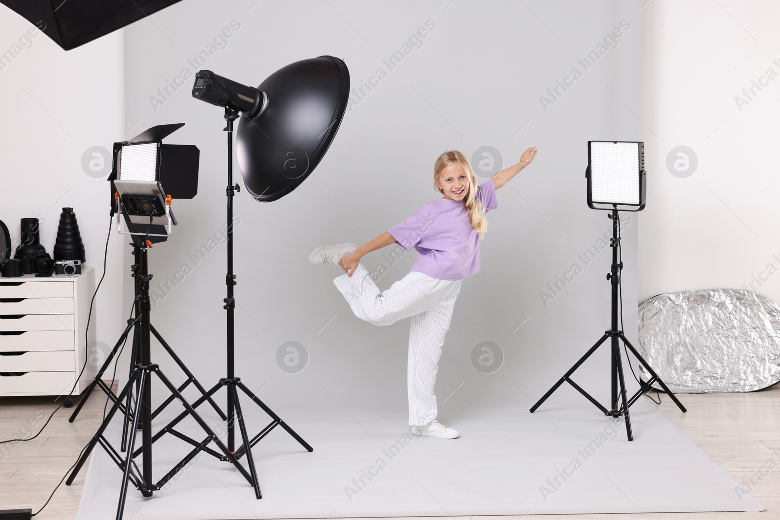 Photo of Little girl on light grey background in photo studio with professional equipment