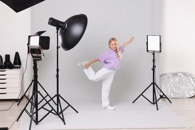 Photo of Little girl on light grey background in photo studio with professional equipment