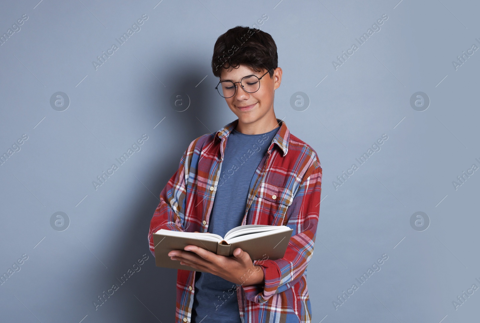 Teenage boy reading book on grey background Photo of Teenage boy reading book on grey background