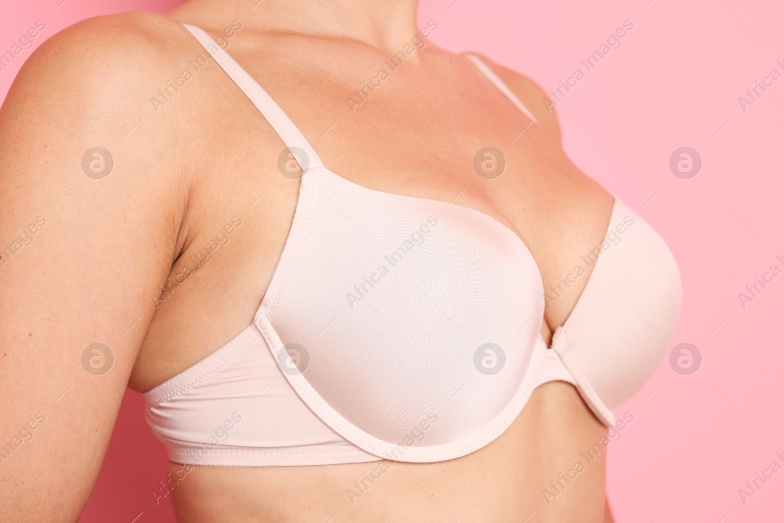 Photo of Woman wearing beautiful beige bra on pink background, closeup