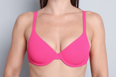 Photo of Woman wearing beautiful pink bra on light grey background, closeup