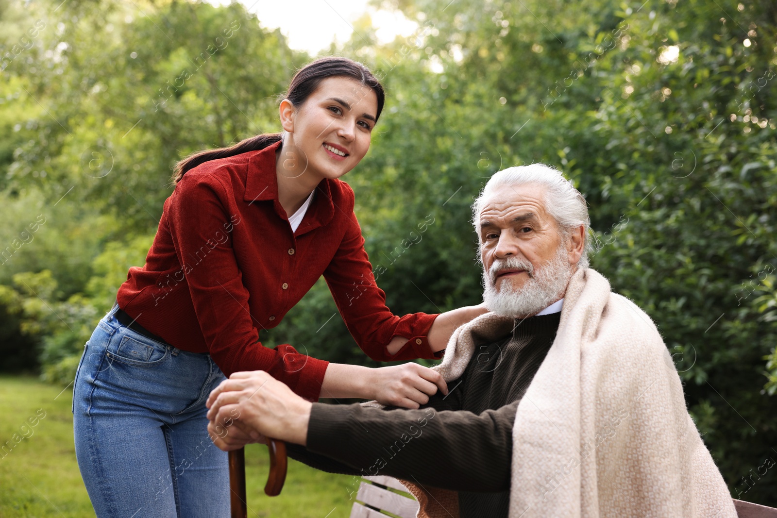 Portrait of smiling caregiver and elderly man with walking cane on bench outdoors Photo of Portrait of smiling caregiver and elderly man with walking cane on bench outdoors