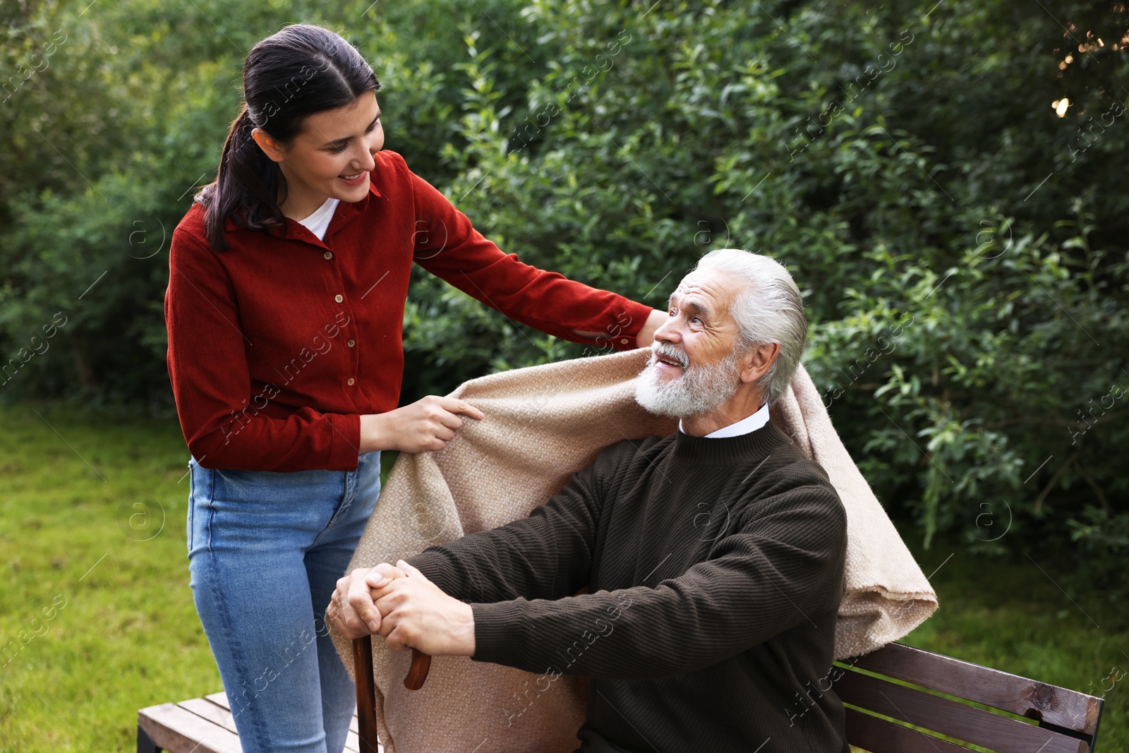 Photo of Smiling caregiver helping elderly man with walking cane outdoors