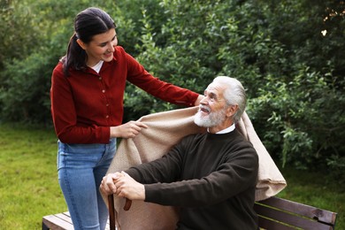 Photo of Smiling caregiver helping elderly man with walking cane outdoors
