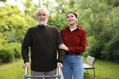 Photo of Smiling caregiver supporting elderly man who using walking frame outdoors