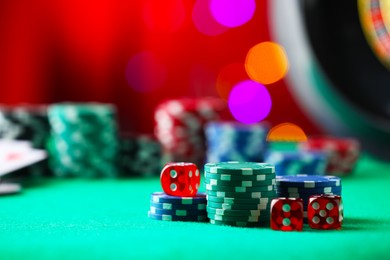Photo of Casino chips and dice on green table against blurred lights, closeup