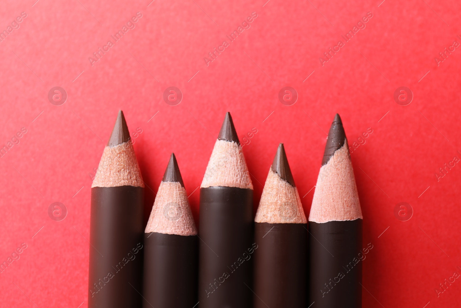 Many eyebrow pencils on red background, flat lay Photo of Many eyebrow pencils on red background, flat lay