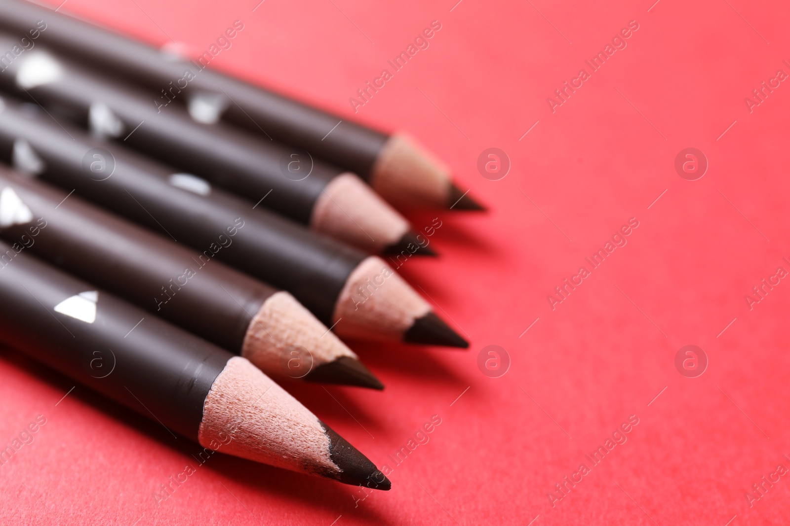 Many eyebrow pencils on red background, closeup. Space for text Photo of Many eyebrow pencils on red background, closeup. Space for text