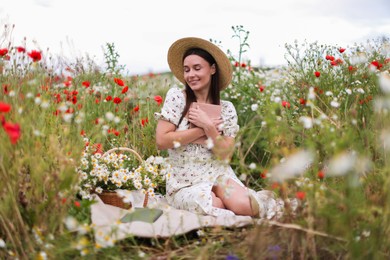 Photo of Smiling woman in hat with book and basket of chamomile flowers in wildflower meadow