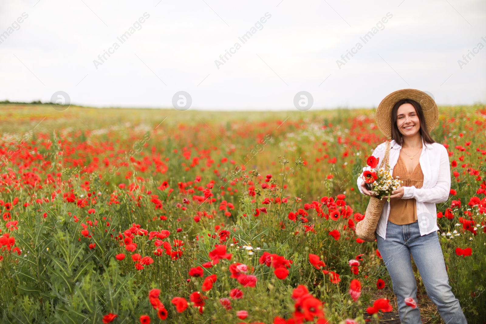 Photo of Smiling woman in hat with bag of wildflowers among poppy flowers in meadow