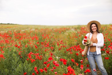Photo of Smiling woman in hat with bag of wildflowers among poppy flowers in meadow