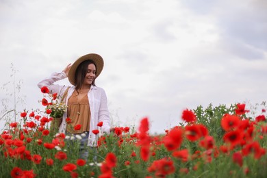 Photo of Smiling woman in hat with bag of wildflowers among poppy flowers in meadow, low angle view