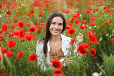 Photo of Portrait of smiling woman among red poppy flowers in wildflower meadow