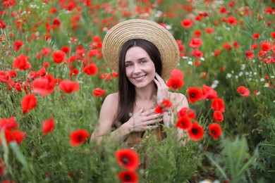 Photo of Portrait of smiling woman in hat among red poppy flowers in wildflower meadow
