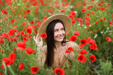 Photo of Smiling woman in hat among red poppy flowers in wildflower meadow