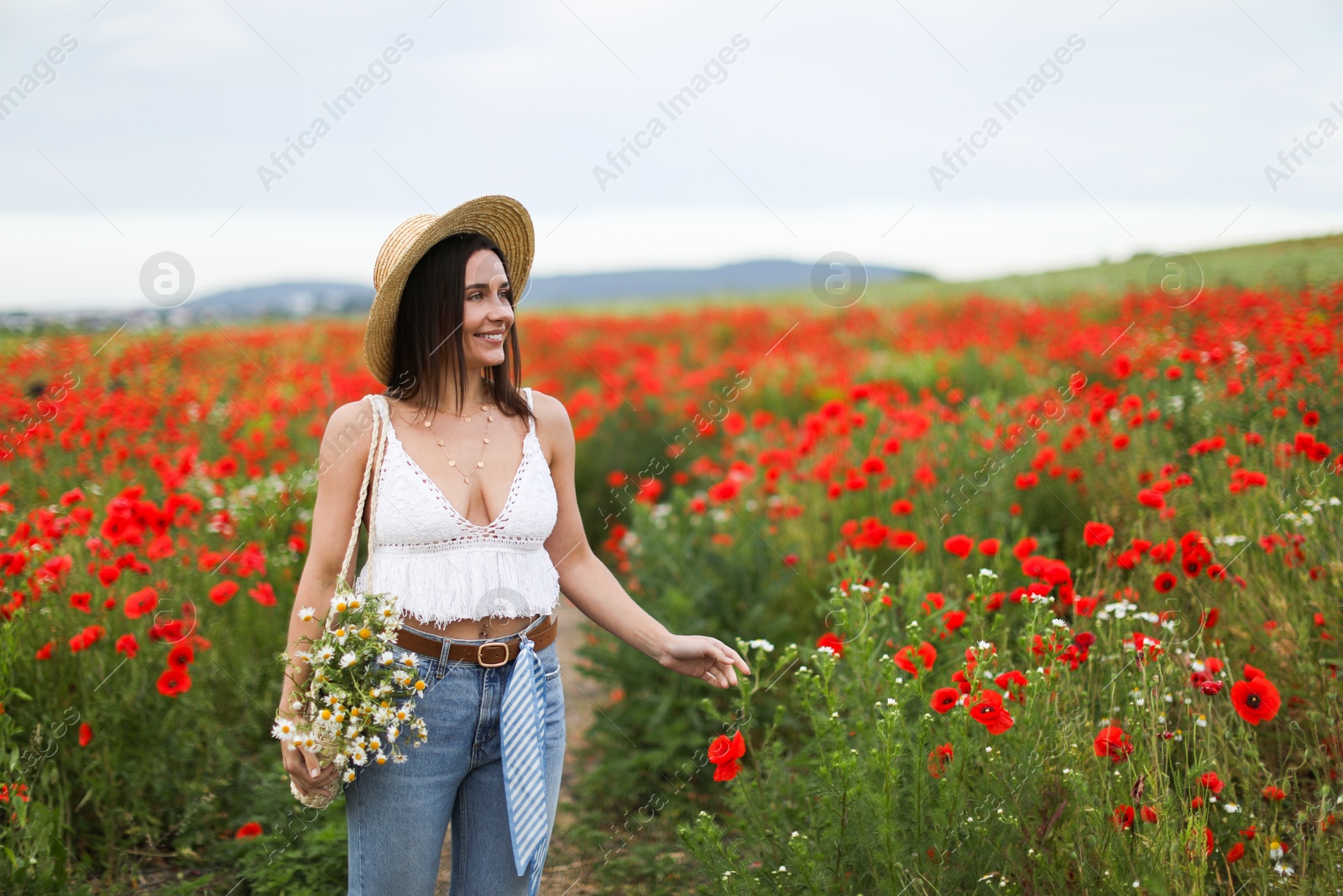 Smiling woman in hat with bag of chamomile flowers in wildflower meadow Photo of Smiling woman in hat with bag of chamomile flowers in wildflower meadow