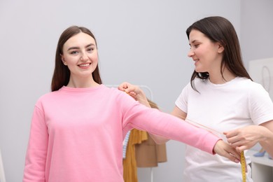 Photo of Tailor measuring woman's arm with tape in atelier