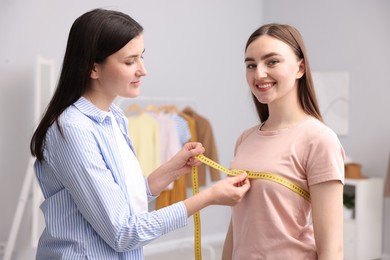 Photo of Tailor measuring woman's chest with tape in atelier