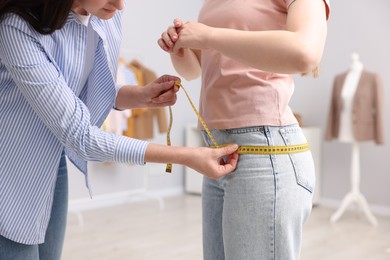 Photo of Tailor measuring woman's hips in atelier, closeup