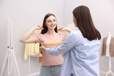 Photo of Tailor measuring woman's chest with tape in atelier