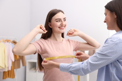 Photo of Tailor measuring woman's chest with tape in atelier