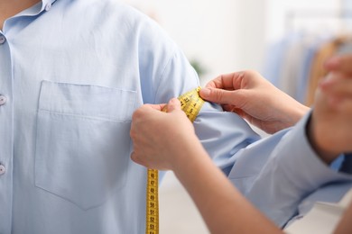 Photo of Tailor measuring woman's arm with tape in atelier, closeup