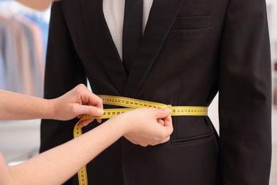 Photo of Tailor measuring jacket on man in atelier, closeup