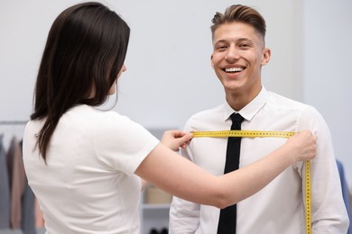 Photo of Tailor measuring man's chest with tape in atelier