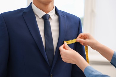 Photo of Tailor measuring jacket on man in atelier, closeup