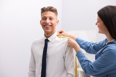 Photo of Tailor measuring woman's arm with tape in atelier