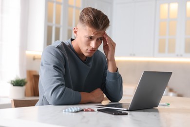 Photo of Sick man having online consultation with doctor via laptop at white marble table in kitchen