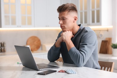 Photo of Sick man having online consultation with doctor via laptop at white marble table in kitchen