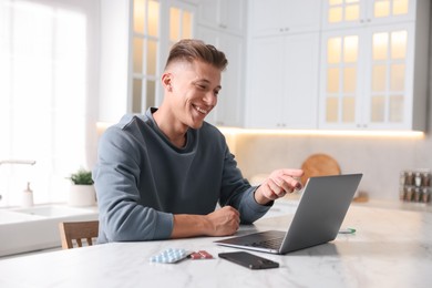 Photo of Sick man having online consultation with doctor via laptop at white marble table in kitchen