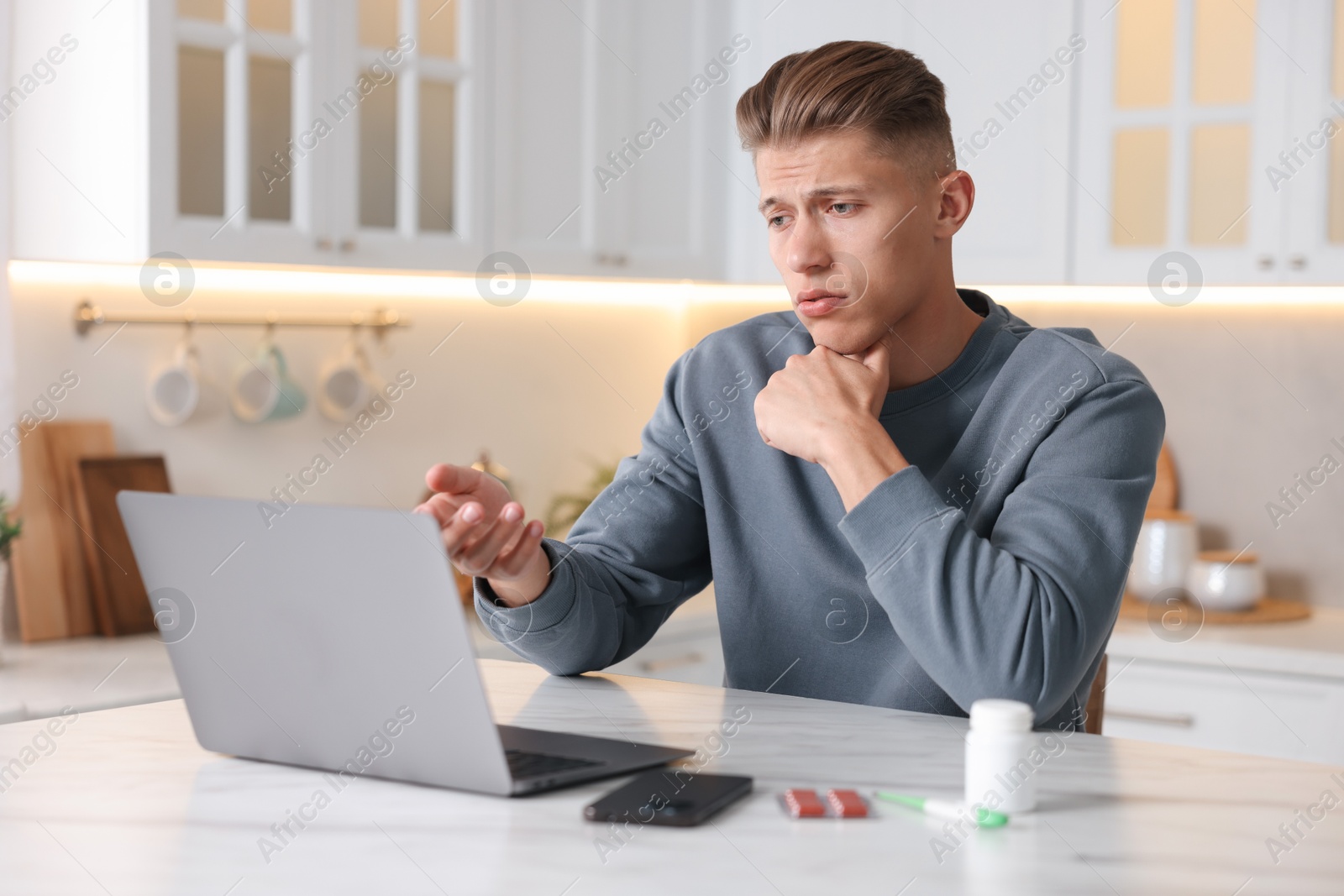 Sick man having online consultation with doctor via laptop at white marble table in kitchen Photo of Sick man having online consultation with doctor via laptop at white marble table in kitchen