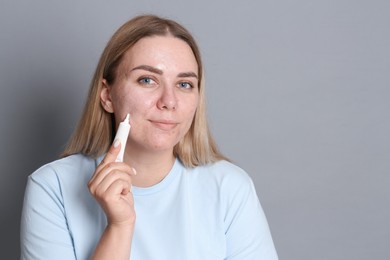 Photo of Woman applying cream onto face on grey background, space for text. Acne treatment
