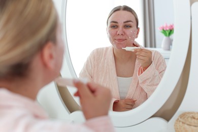 Photo of Woman applying cream onto face near mirror indoors. Acne treatment