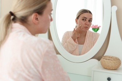Photo of Woman with acne problem looking in mirror at home