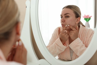 Photo of Woman with acne problem looking in mirror at home