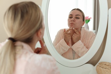 Photo of Woman with acne problem looking in mirror at home