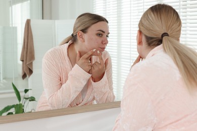 Photo of Woman popping pimple near mirror in bathroom. Acne problem