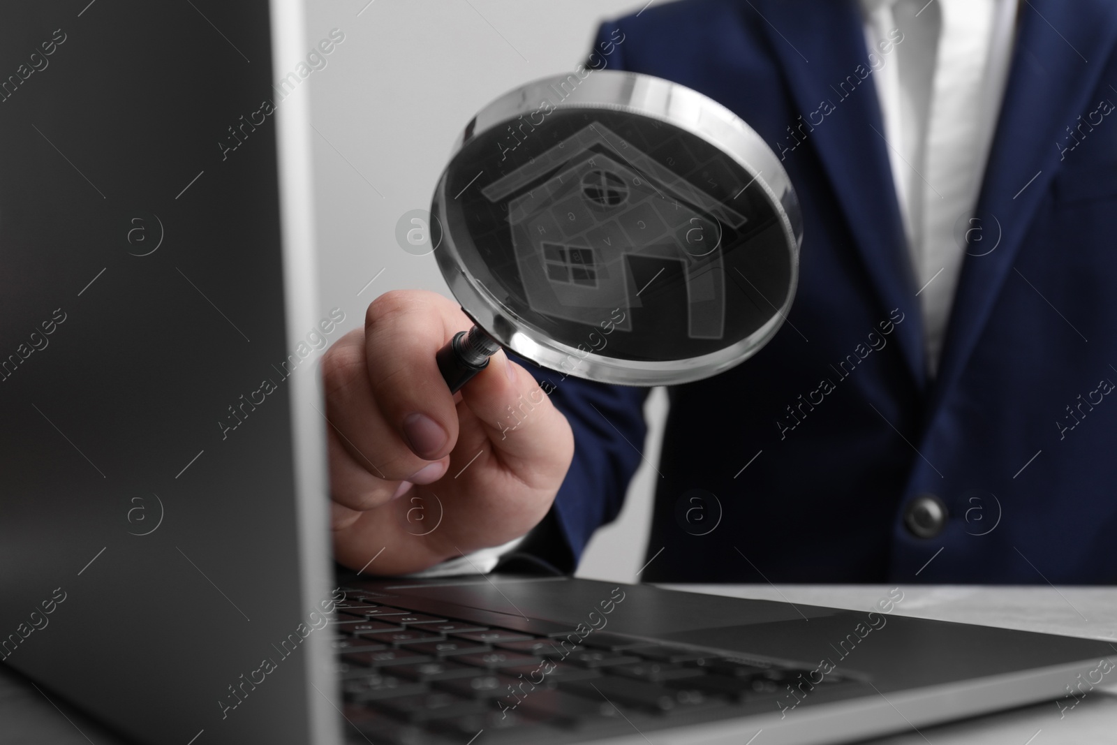 Real estate agent holding magnifying glass with house icon inside above laptop, closeup Image of Real estate agent holding magnifying glass with house icon inside above laptop, closeup
