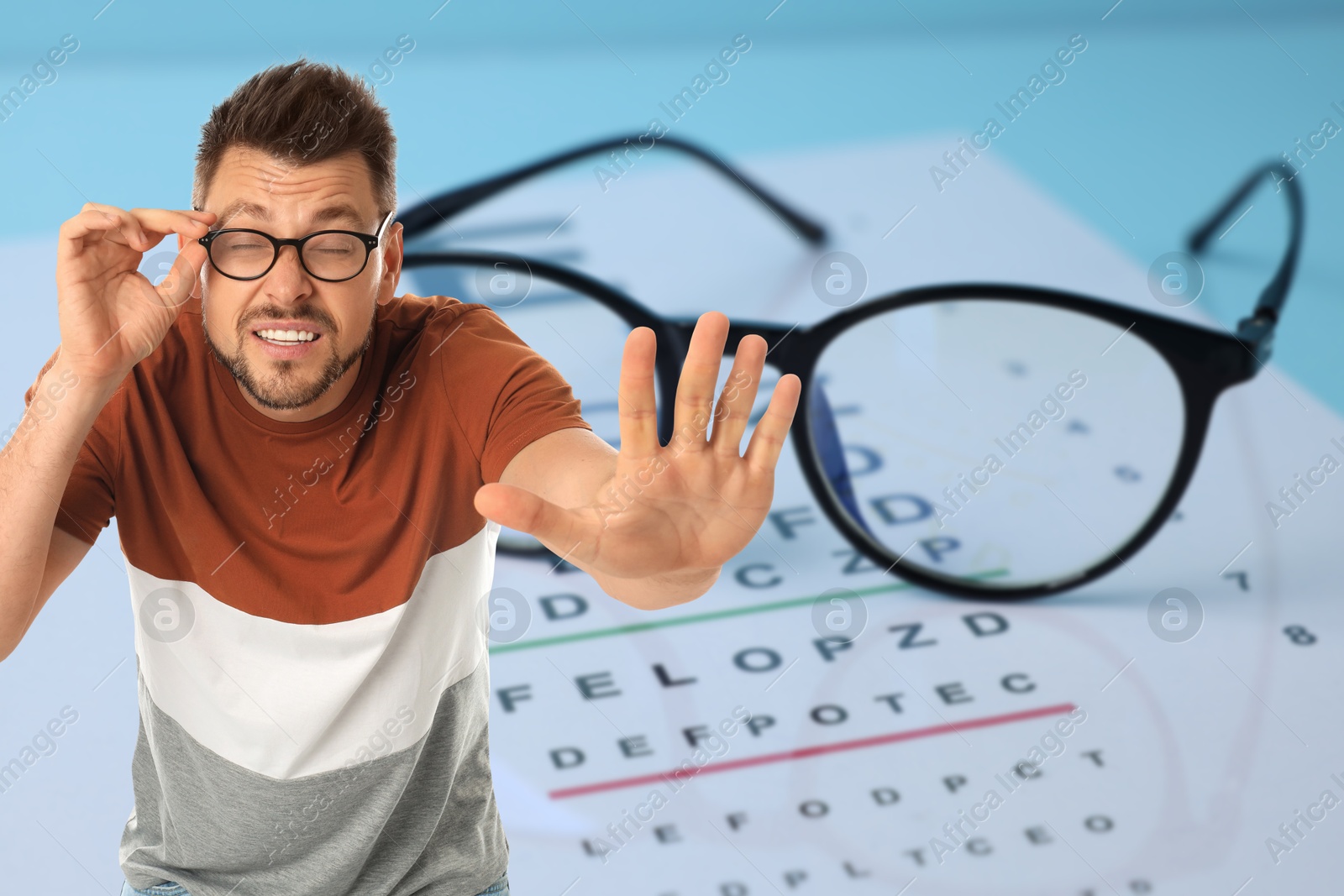 Man with eyesight problems, glasses and vision test chart on light blue background Image of Man with eyesight problems, glasses and vision test chart on light blue background
