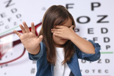 Image of Little girl with eyesight problems, glasses and vision test chart
