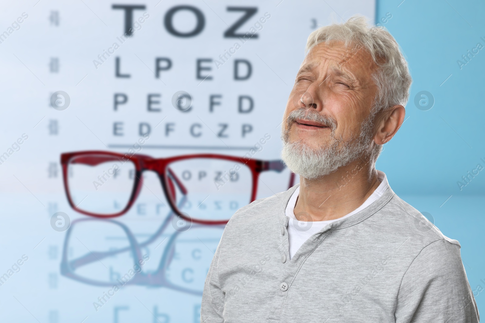 Senior man with eyesight problems, glasses and vision test chart on light blue background Image of Senior man with eyesight problems, glasses and vision test chart on light blue background