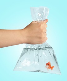 Image of Woman holding plastic bag with water and goldfish against light blue background, closeup