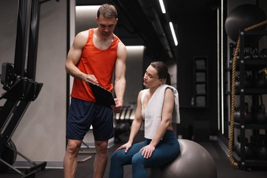 Photo of Young woman with professional personal trainer in gym